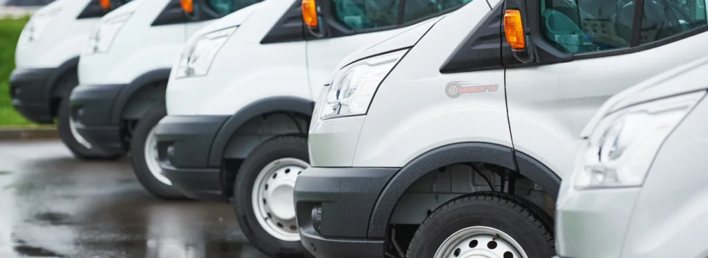 Fleet of service vans parked outside an auto repair shop offering commercial account maintenance for plumbing, HVAC, and delivery businesses